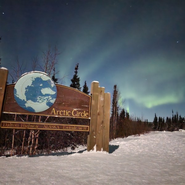 Northern lights glowing above Arctic Circle sign along Dalton Highway Alaska
