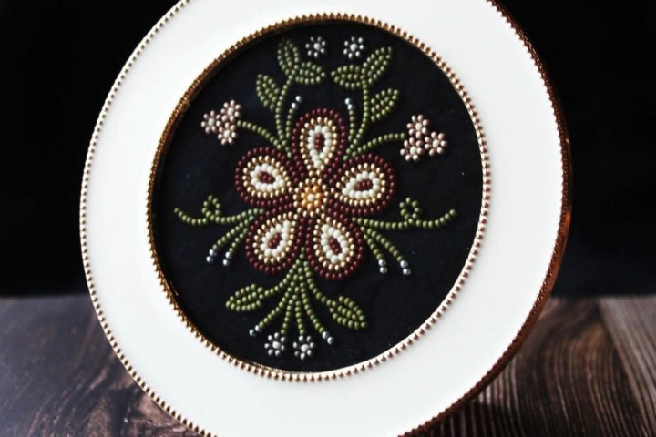 Round embroidery with floral pattern displayed in white frame on wooden surface.