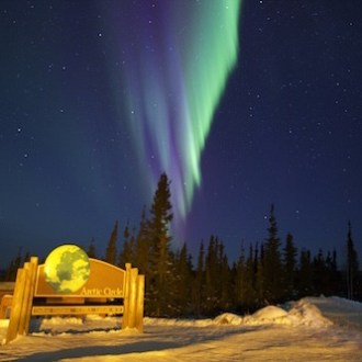 Northern lights glowing over Arctic Circle sign along Dalton Highway Alaska