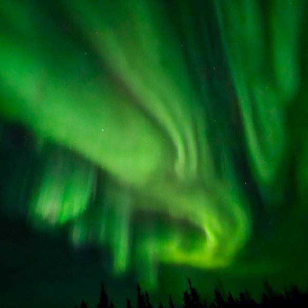 Green and purple northern lights stretching across winter sky in Alaska