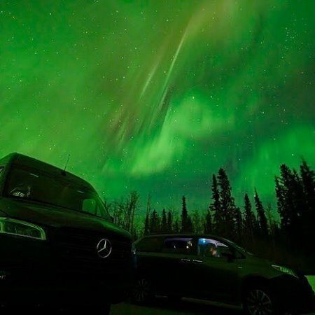 Purple and green northern lights reflecting over a moving car near Fairbanks Alaska