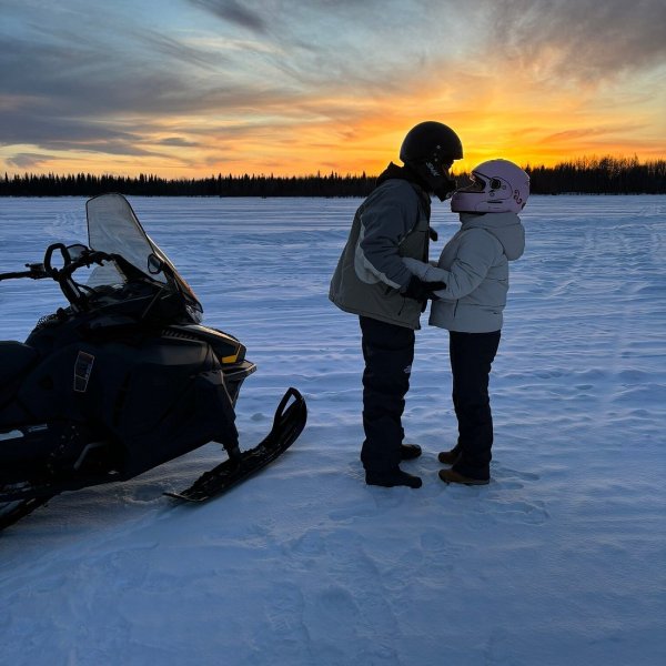 Couple kissing beside snowboard in snowy landscape during Alaska Wild Lights tour