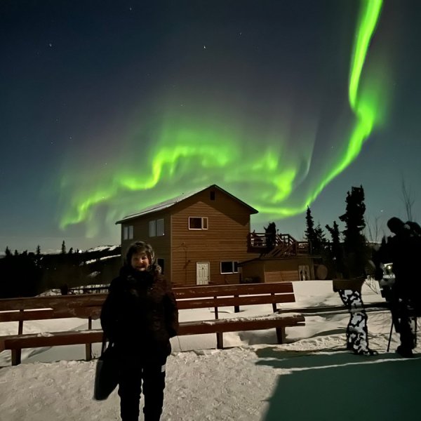 Northern lights glowing above roof with man standing in foreground
