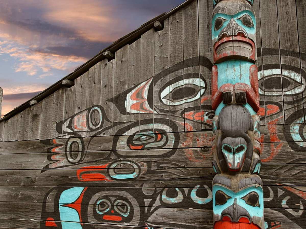 Wooden totem pole and wall art against a cloudy sky background.