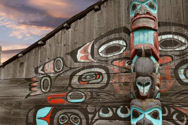 Wooden totem pole and wall art against a cloudy sky background.