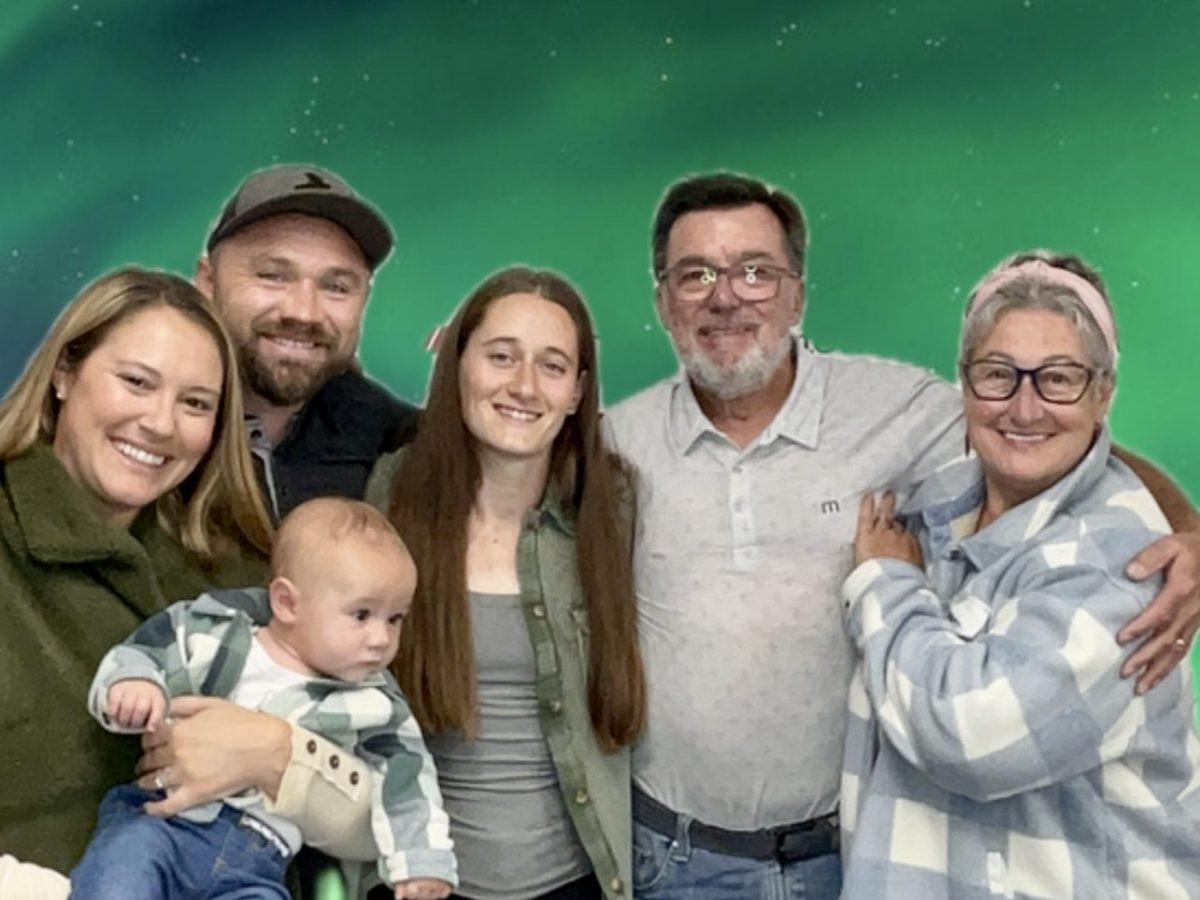 Family of six posing under green northern lights, including a baby.
