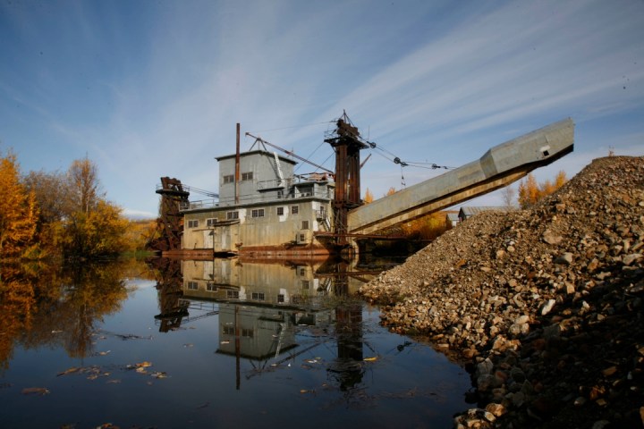 Old dredge by a pond with autumn trees and clear sky reflection in water.