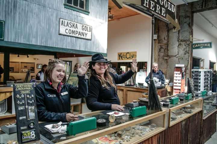 Two people waving behind a counter at Alaska Gold Company souvenir shop.