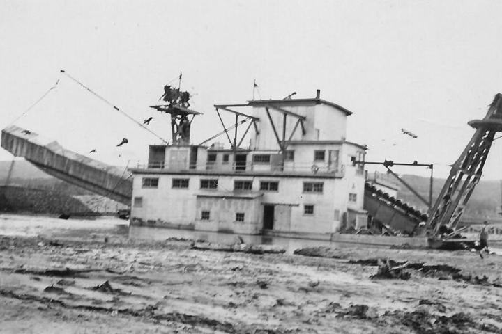 Old industrial dredging machine on a riverbank with conveyor belts and cables.