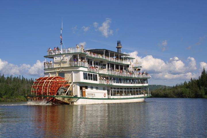 Paddle steamer on a river with trees in the background under a clear blue sky.