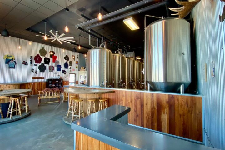 Interior of a brewery with stainless steel tanks, rustic wooden bar, and wall display of shirts.