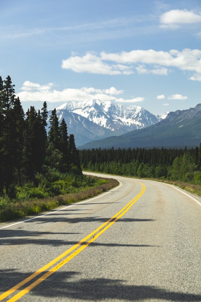 Scenic highway winding through spruce forest toward snow-capped mountains in Alaska