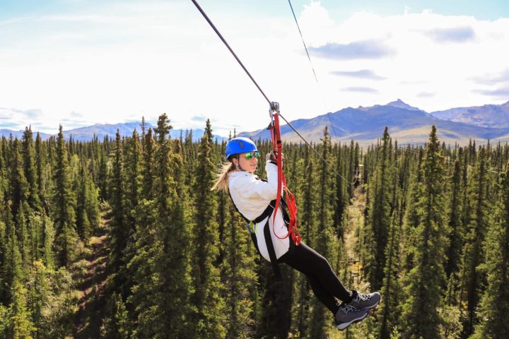 Person ziplining over a forested area with mountains in the background, wearing a helmet and harness.