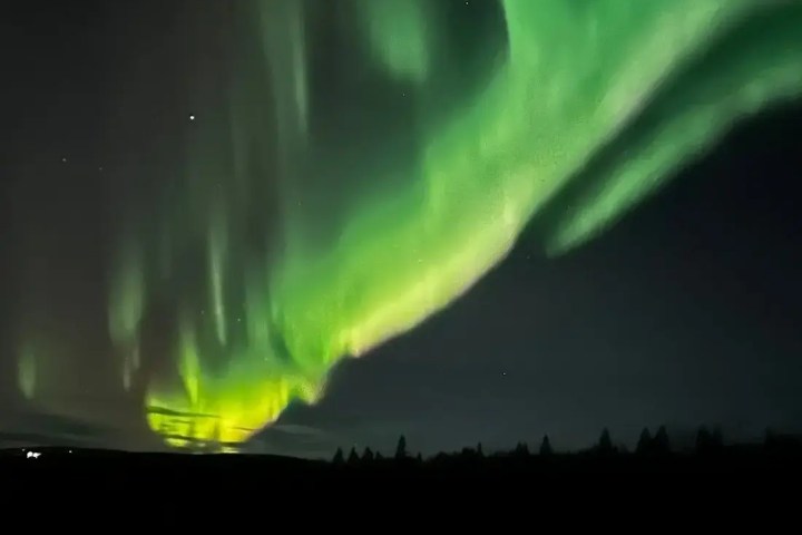 Green aurora borealis lights illuminating a dark night sky over a snowy landscape.