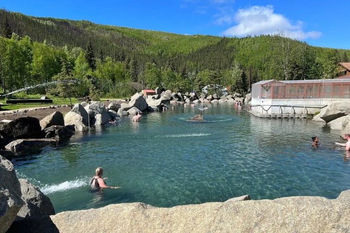 People swimming in a natural hot spring pool surrounded by rocks and trees.
